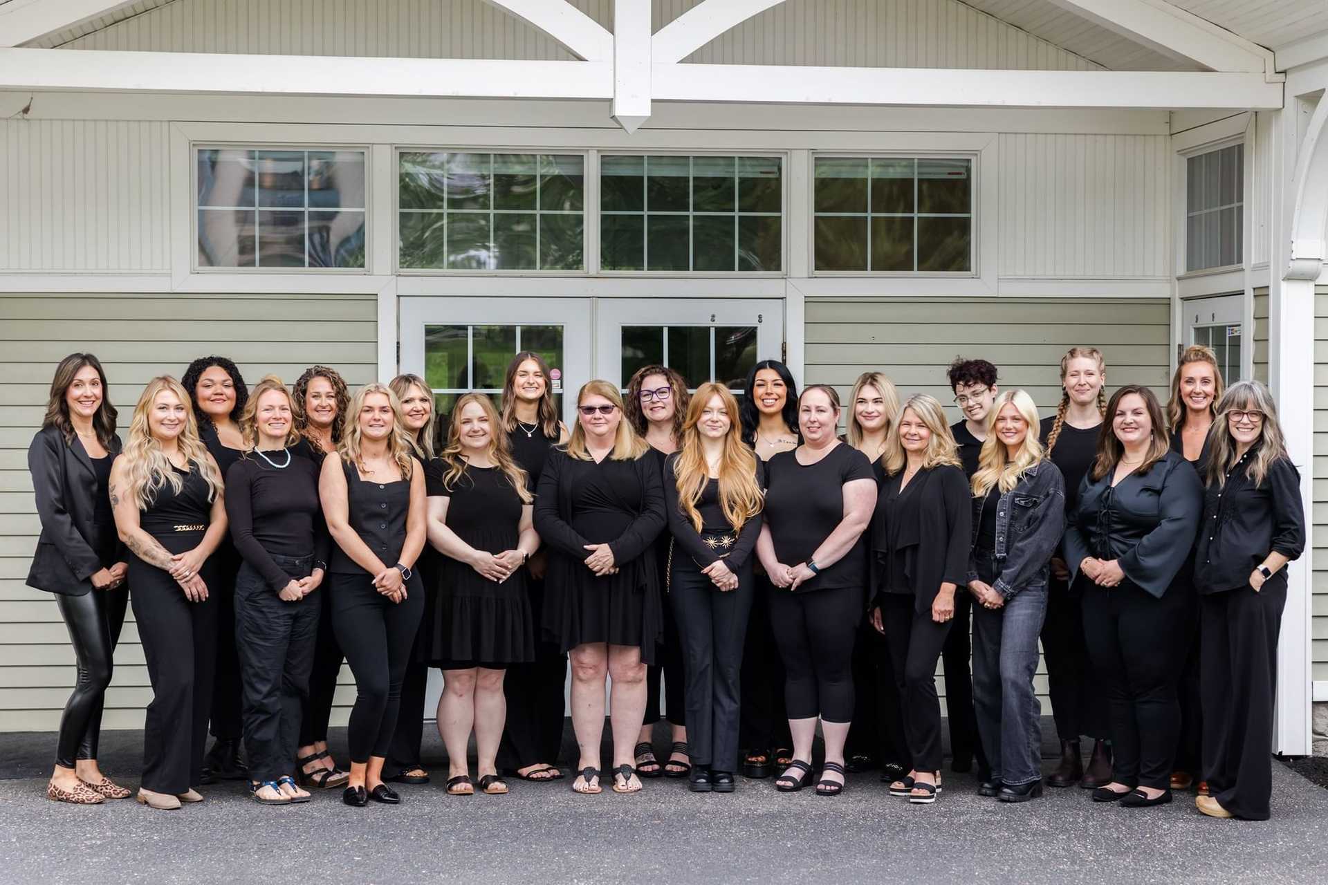 Group of 19 women in black outfits standing outside a building.