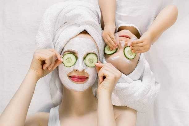 Two people with towels on heads enjoying face masks with cucumber slices on eyes.